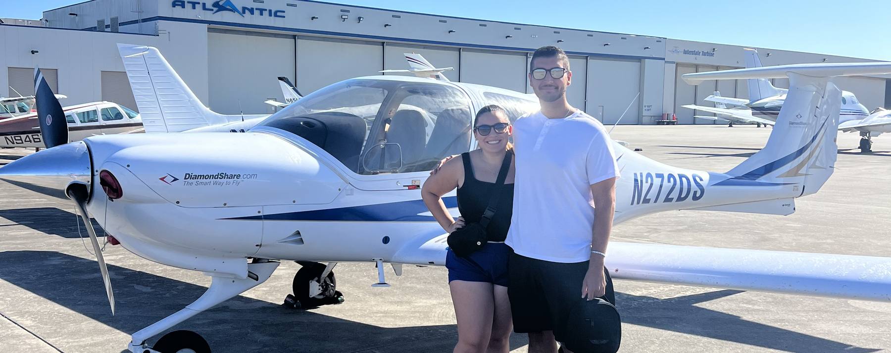 Nick and Kim standing together beside a small white airplane on the tarmac